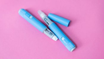 Close-up of two blue insulin pens on a pink background. Medical device for diabetes treatment, used for injecting insulin to control blood sugar levels. Healthcare and chronic illness concept.