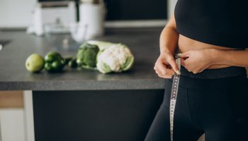 Young woman with measuting tape on weist at the kitchen